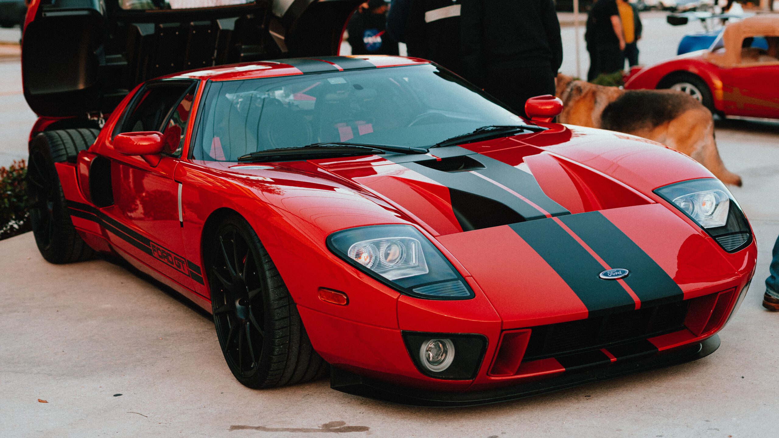 heros-img A striking red Ford GT parked outdoors at a car show, attracting a crowd.